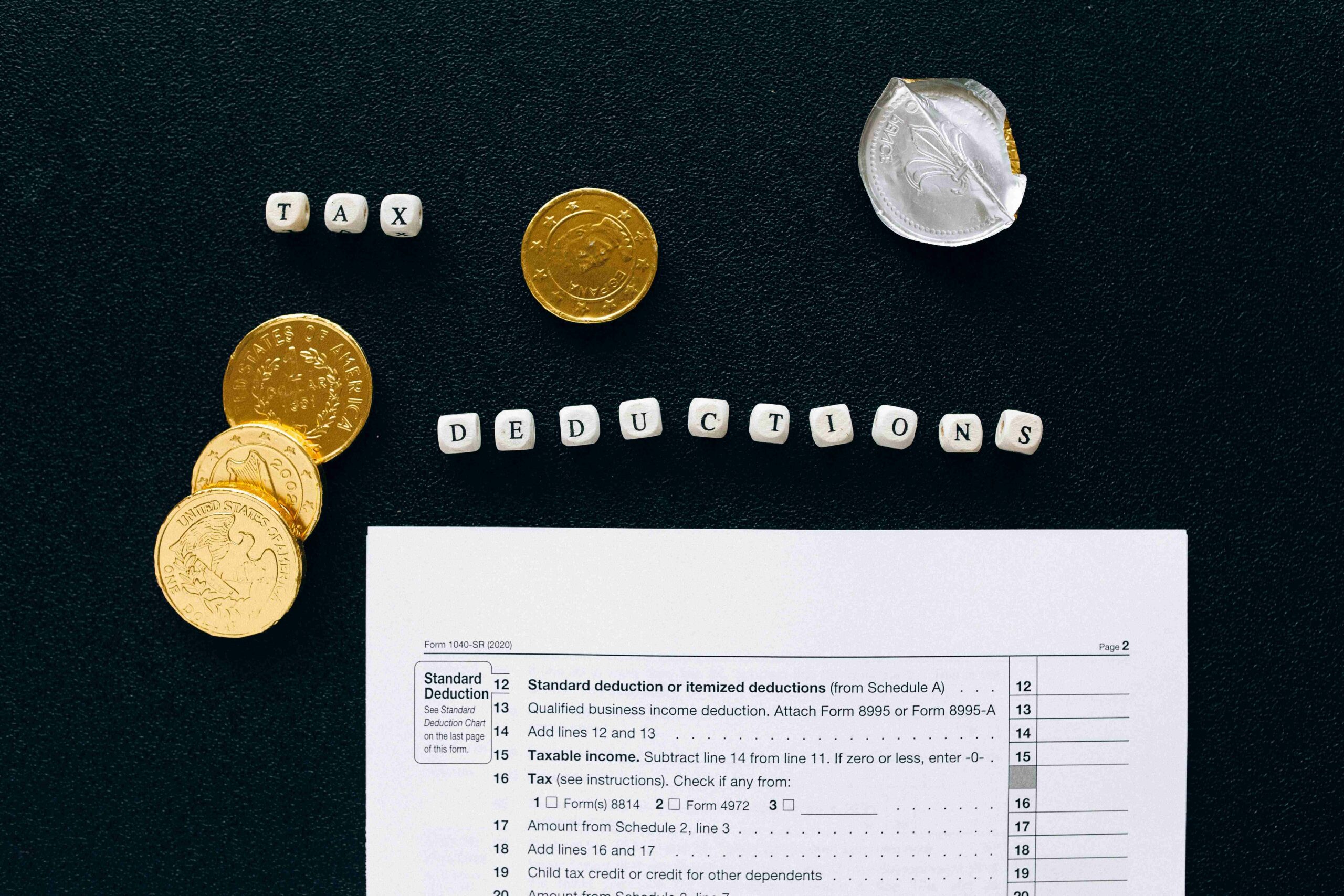 A piece of paper with coins around it and above it is a group of dices that spell "tax deduction"