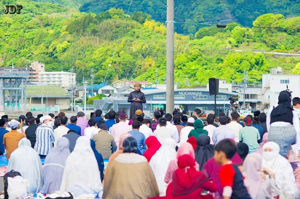 a preacher in black robe speaking before a large group of Muslims, which highlights the positive sentiment towards Islam in Japan