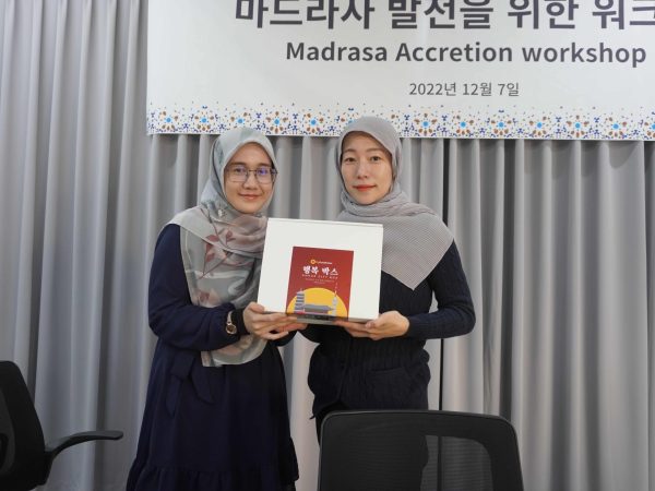 two women, one from MyFundAction organization on the left and a korean on the right, holding a box containing the Quran, and they are posing for a photo